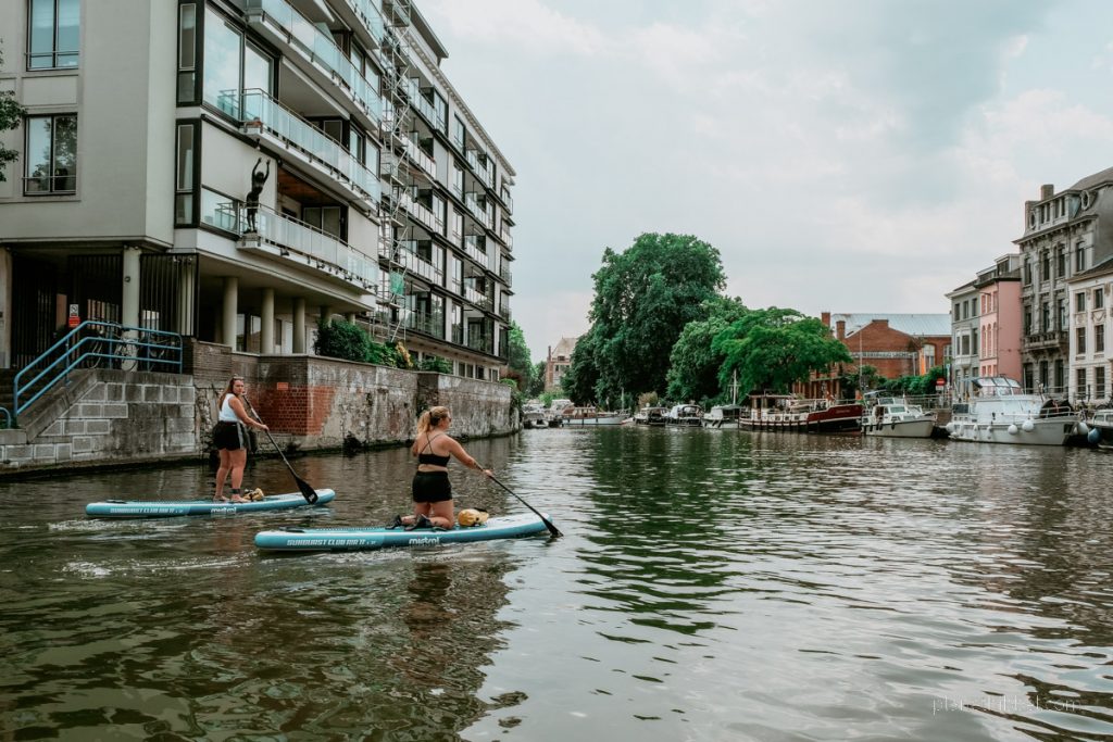 Zwei Frauen auf SUPs, die über die Leie in Gent fahren. 
