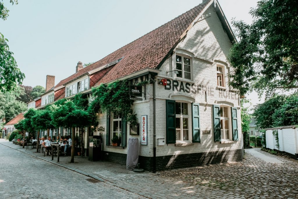 Außenfassade eines Hotel-Restaurants  mit Terrasse, Schirmen, Bestuhlung und Gästen in Deurle. 