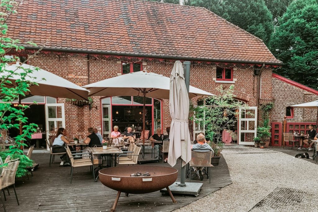 Außenterrasse mit Schirmen, Bestuhlung, Feuerschale und Gästen des Grand Café Het Koetshuis.