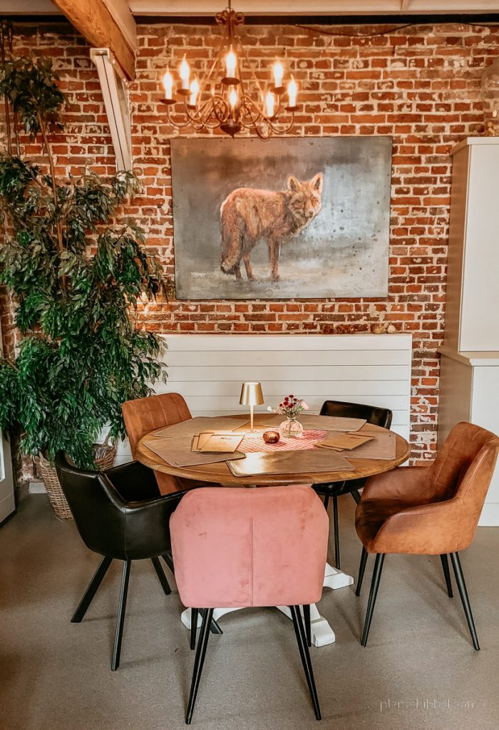 Innenraum des Grand Café Het Koetshuis mit Tisch, Bestuhlung und Bild mit Fuchs vor Backsteinwand. 
