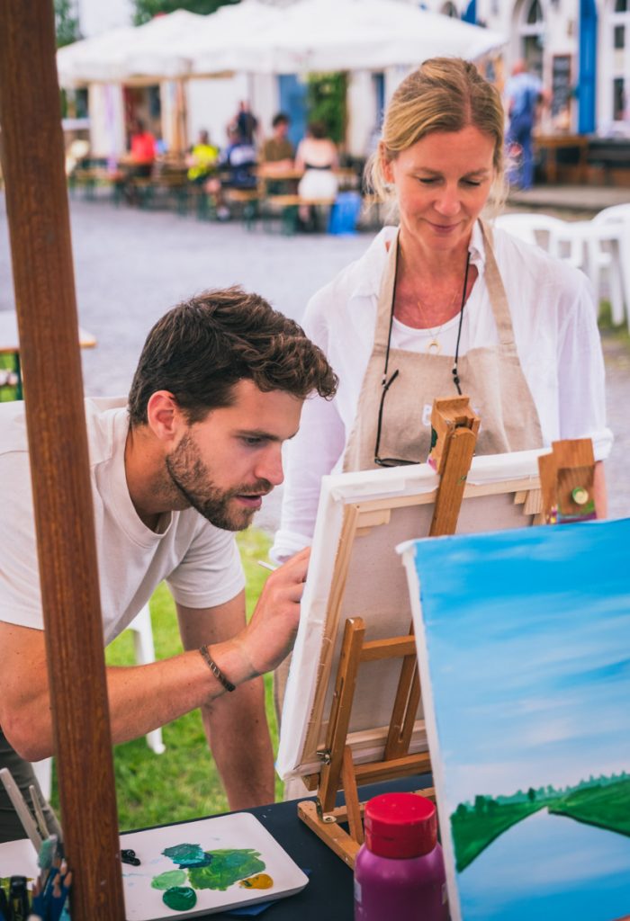 Kunstlehrer und Frau vor Leinwand, die bemalt wird.