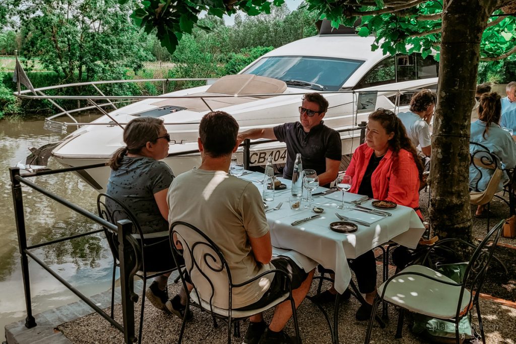 Terrasse des Restaurant Nenuphar mit Blick auf Tisch, Gäste und ein Boot, dass am hauseigenen Steg angelegt hat. 