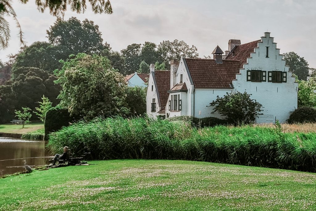 Weiße Villa an der Leie in Sint-Martens-Laatem. Im Vordergrund Wiese mit einem Angler. 