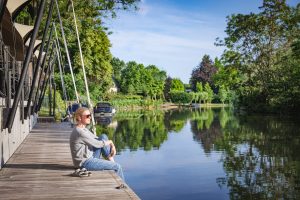 Sitzende Frau auf Steg an einem Fluss